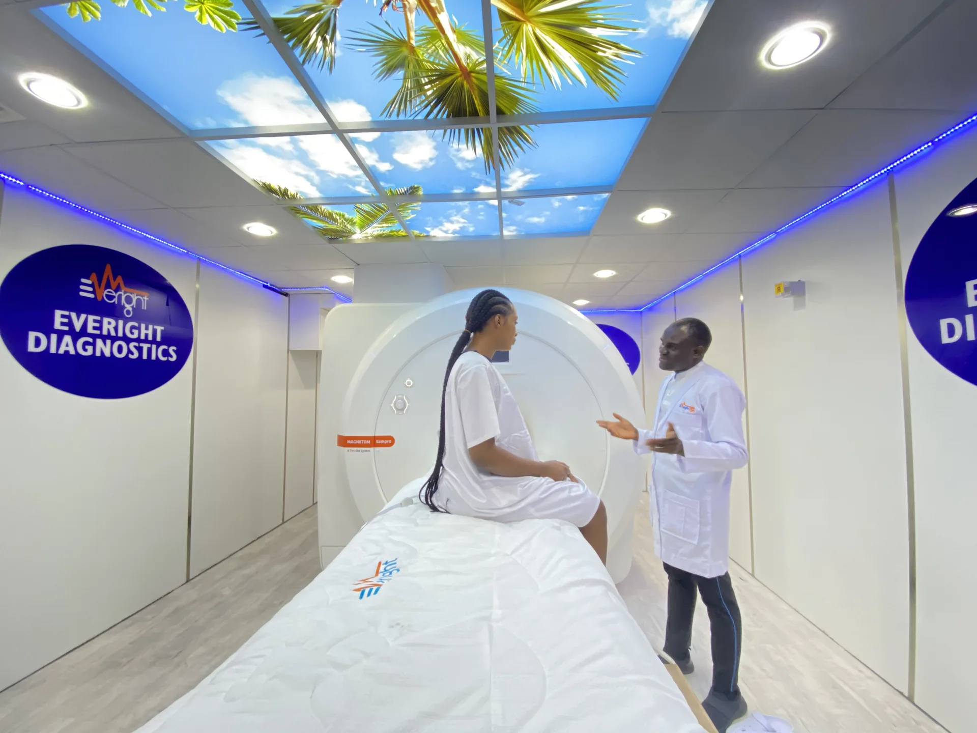 A patient seated on the scanner bed of Everight's 1.5 Tesla Siemens MAGNETOM MRI while a radiographer explains the examination